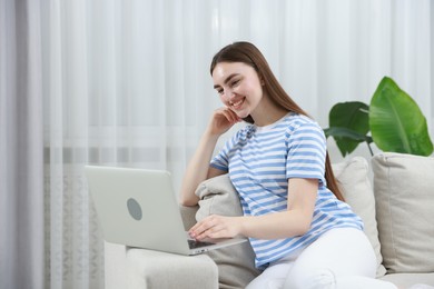 Photo of Young woman using laptop on sofa at home