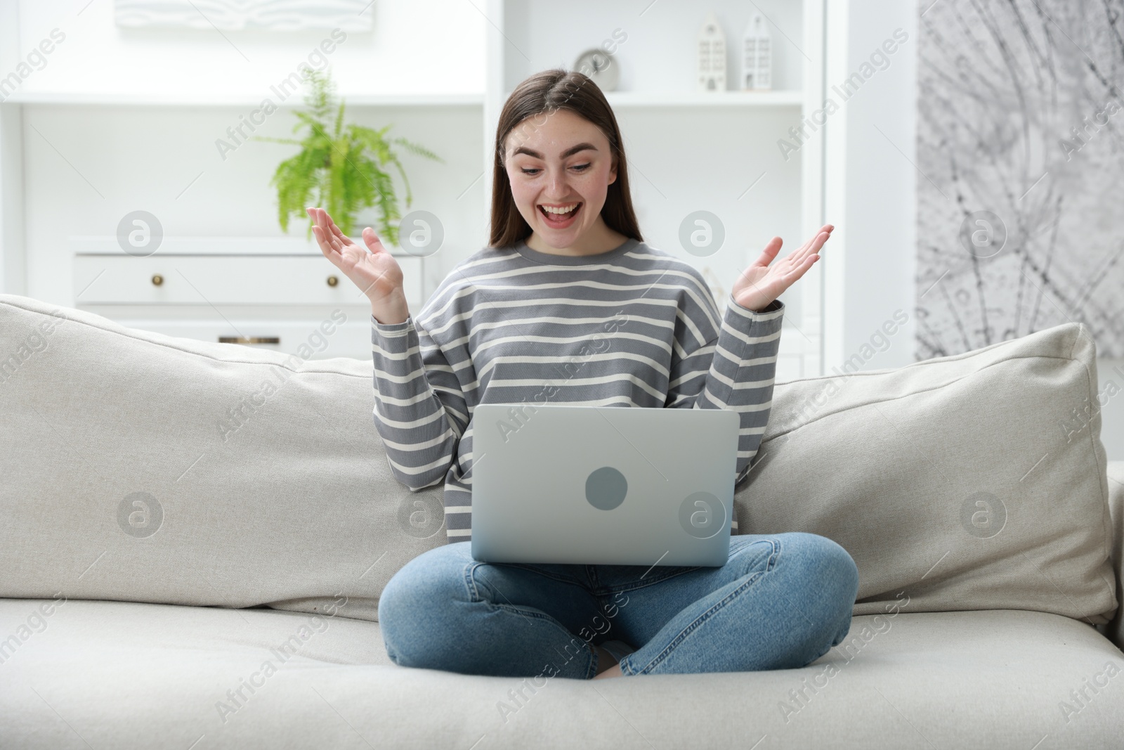 Photo of Emotional young woman with laptop on sofa at home