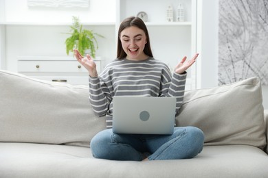 Emotional young woman with laptop on sofa at home