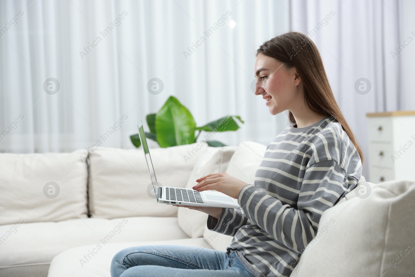 Photo of Young woman using laptop on sofa at home. Space for text