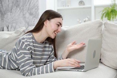 Photo of Happy young woman having video chat via laptop on sofa at home