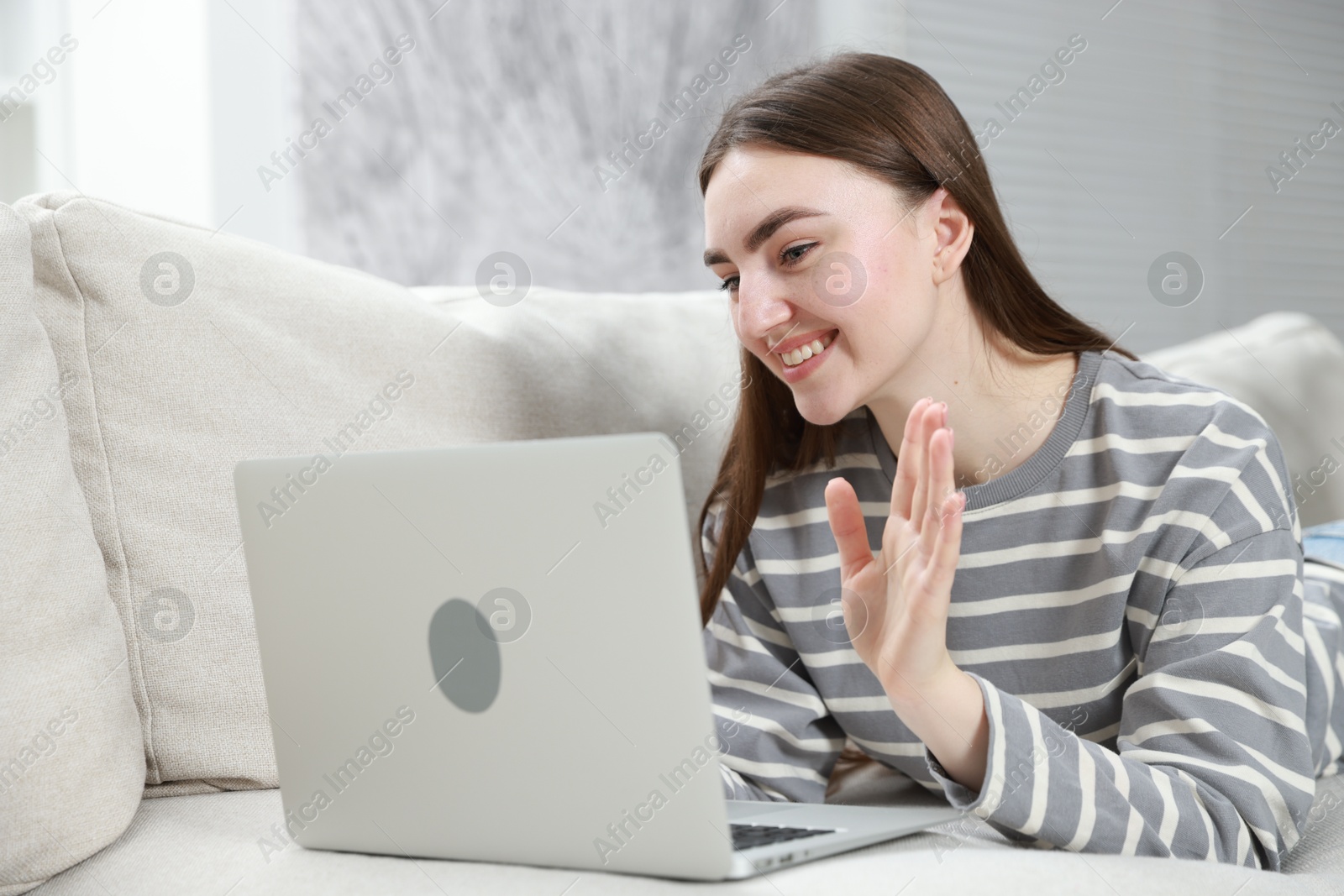 Photo of Happy young woman having video chat via laptop on sofa at home