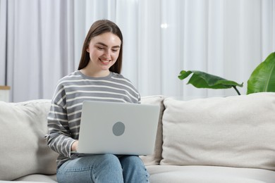 Photo of Young woman using laptop on sofa at home. Space for text