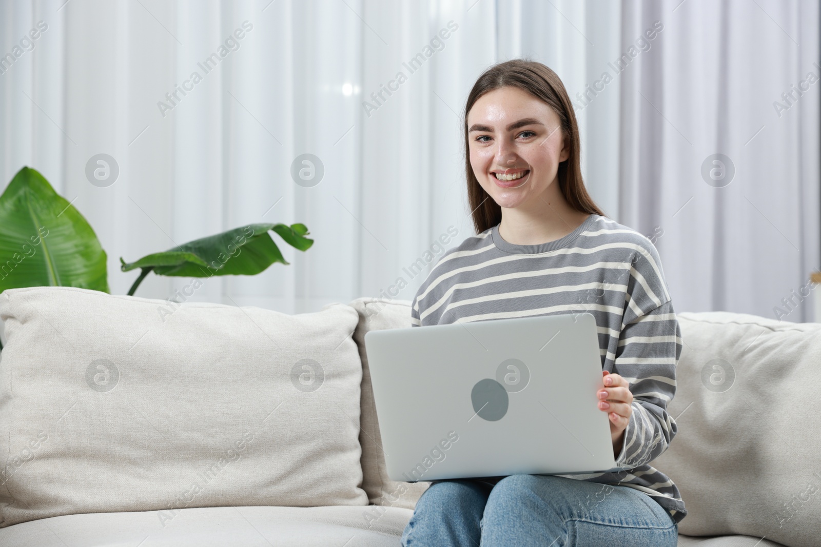 Photo of Young woman using laptop on sofa at home. Space for text