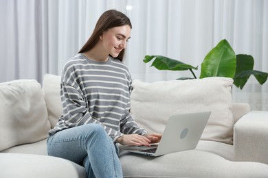 Photo of Young woman using laptop on sofa at home