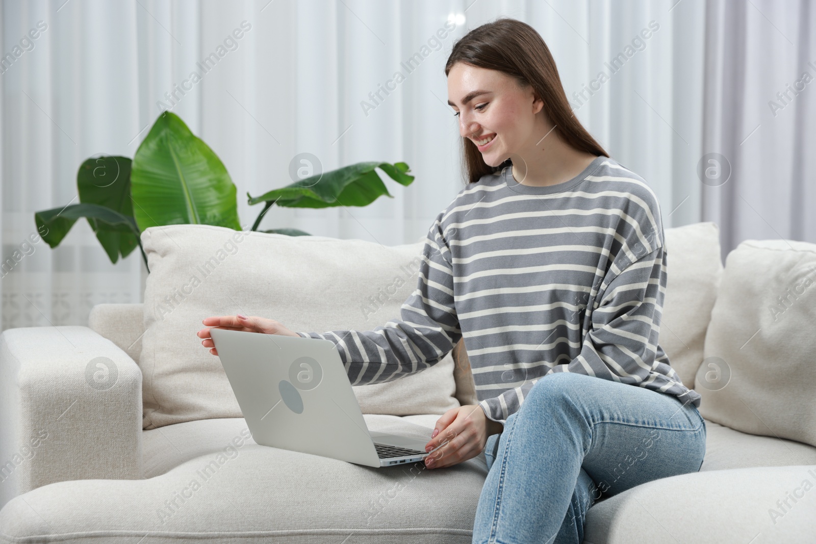 Photo of Young woman using laptop on sofa at home