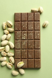 Photo of Delicious Dubai chocolate with pistachios and knafeh on green background, flat lay