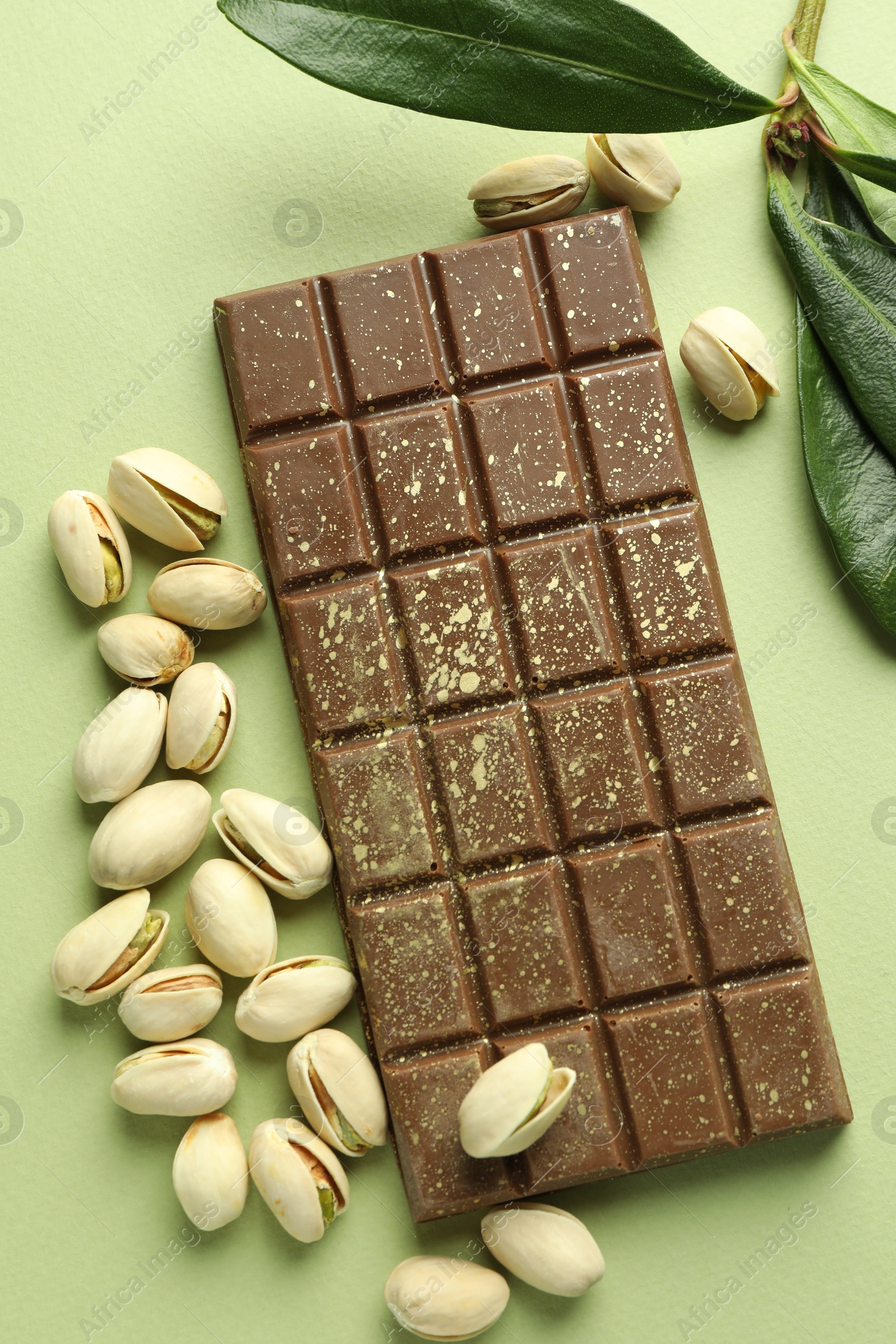 Photo of Delicious Dubai chocolate with pistachios and knafeh on green background, flat lay