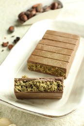 Pieces of delicious Dubai chocolate with pistachios, knafeh and cocoa beans on light textured table, closeup