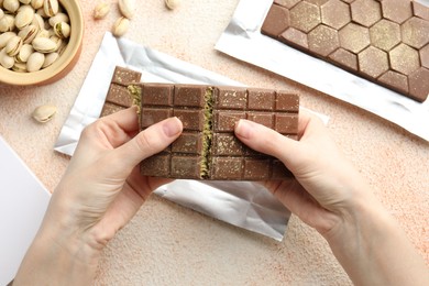 Photo of Woman breaking delicious Dubai chocolate bar with pistachios and knafeh at color textured table, top view