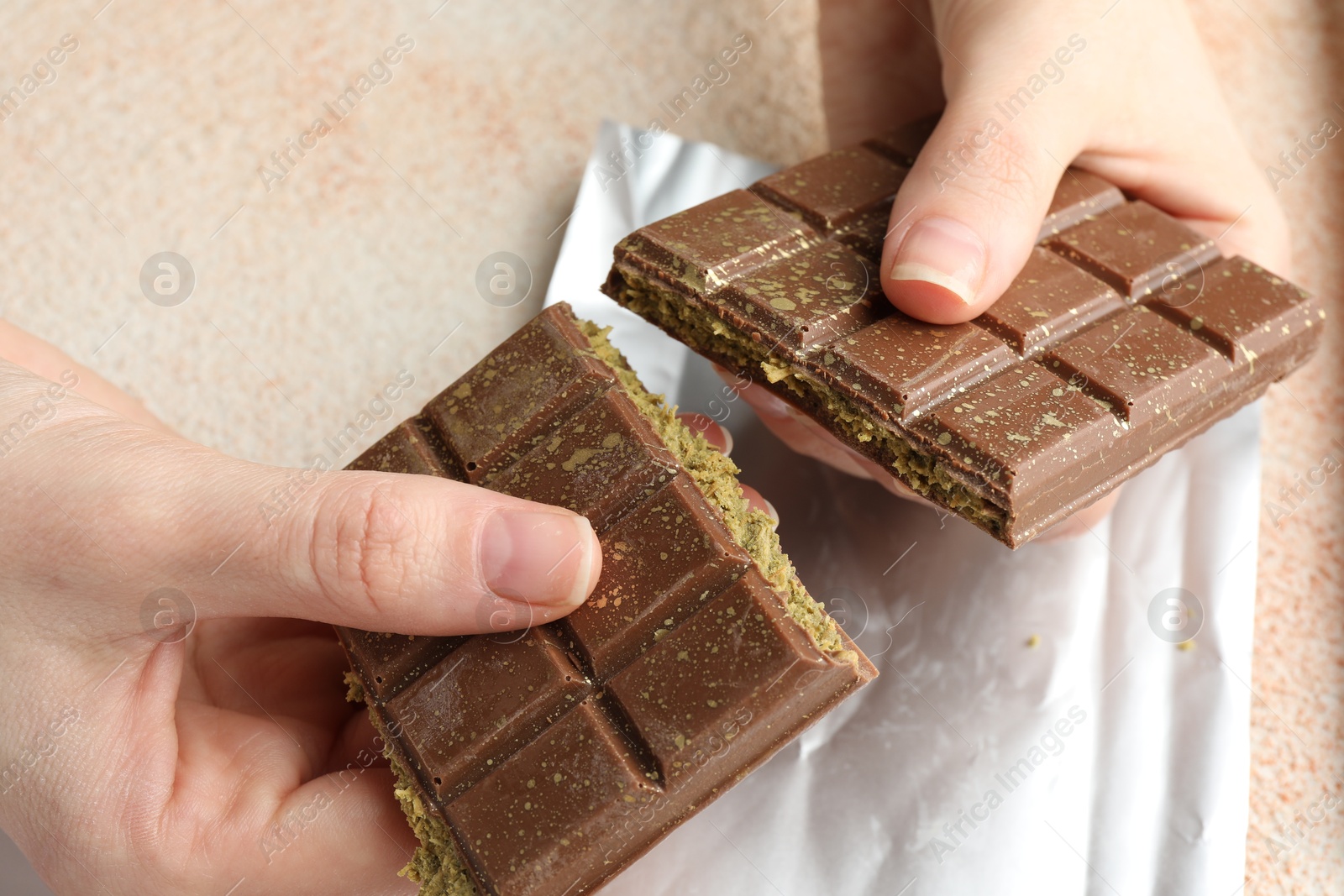 Photo of Woman breaking delicious Dubai chocolate bar with pistachios and knafeh at color textured table, closeup