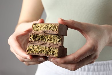 Woman holding pieces of delicious Dubai chocolate with pistachios and knafeh on grey background, closeup