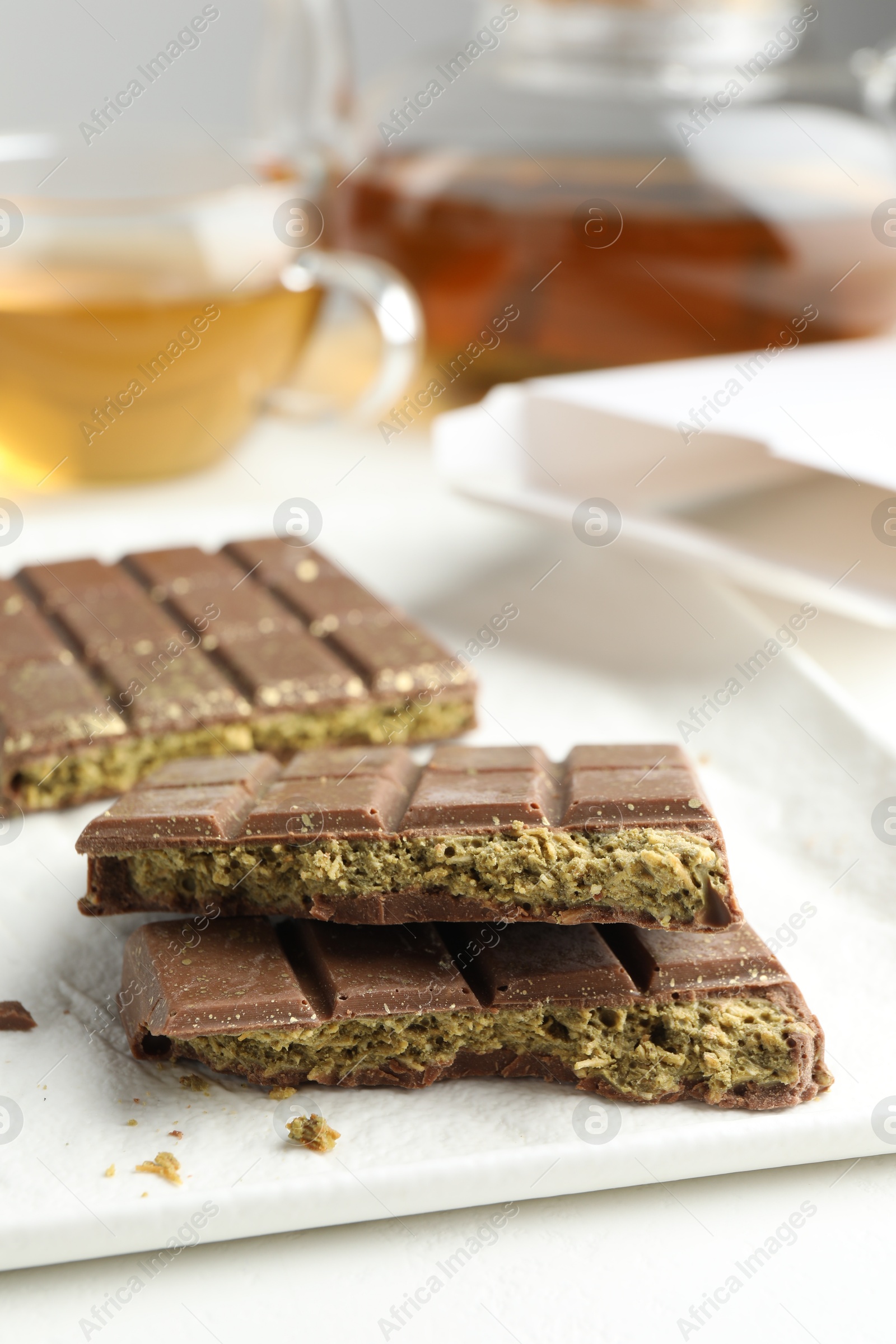 Photo of Pieces of delicious Dubai chocolate with pistachios and knafeh on white table, closeup