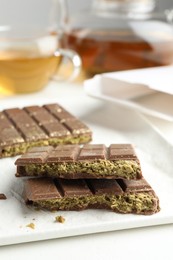 Photo of Pieces of delicious Dubai chocolate with pistachios and knafeh on white table, closeup