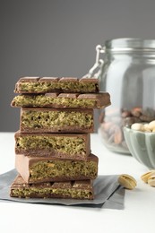 Photo of Pieces of delicious Dubai chocolate with pistachios, knafeh and cocoa beans on white table, closeup