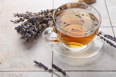 Aromatic lavender tea in glass cup and dry flowers on white tiled table, closeup