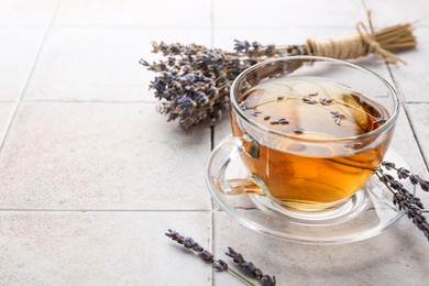 Aromatic lavender tea in glass cup and dry flowers on white tiled table, closeup. Space for text