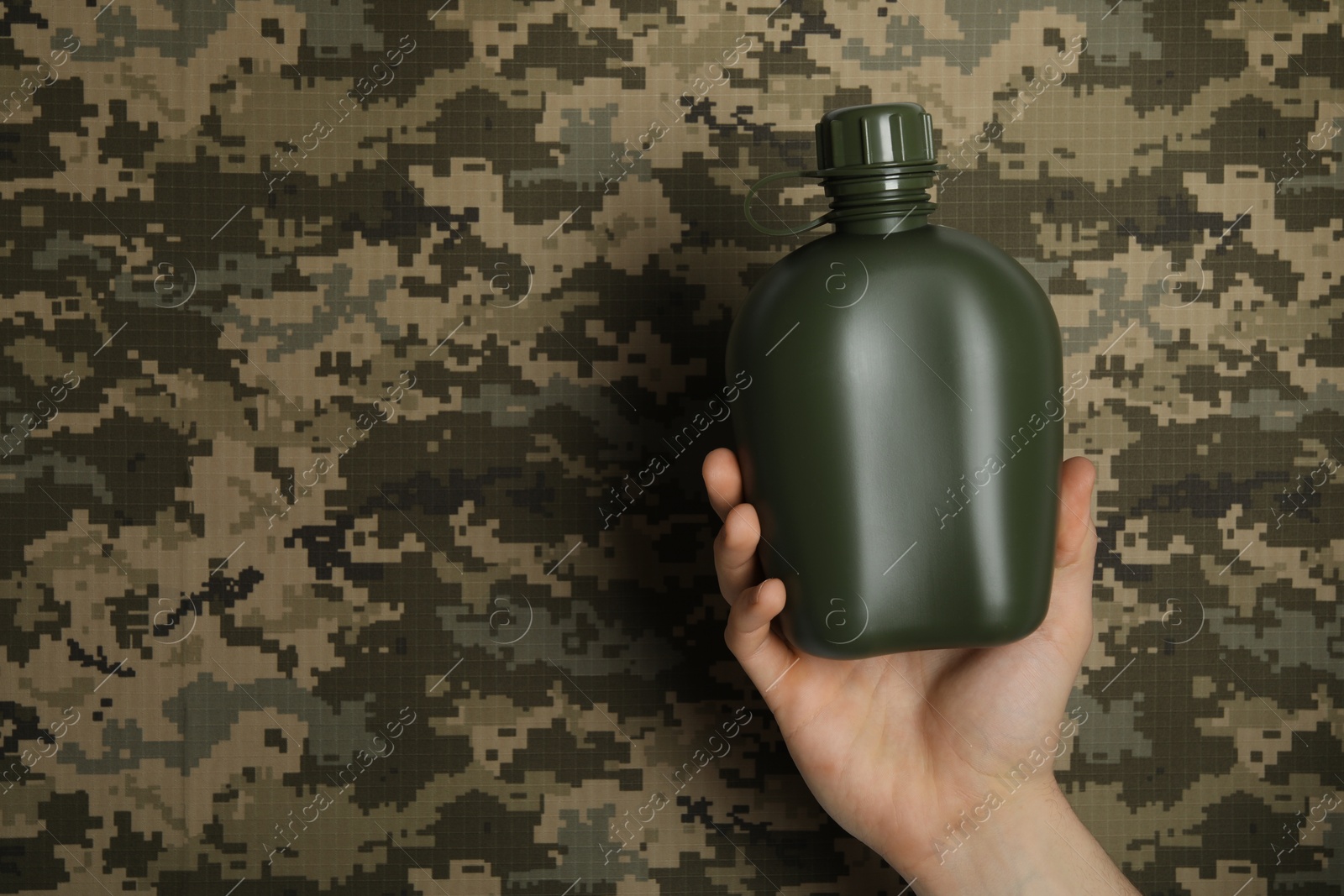 Photo of Man holding green plastic canteen on camouflage background, closeup. Space for text