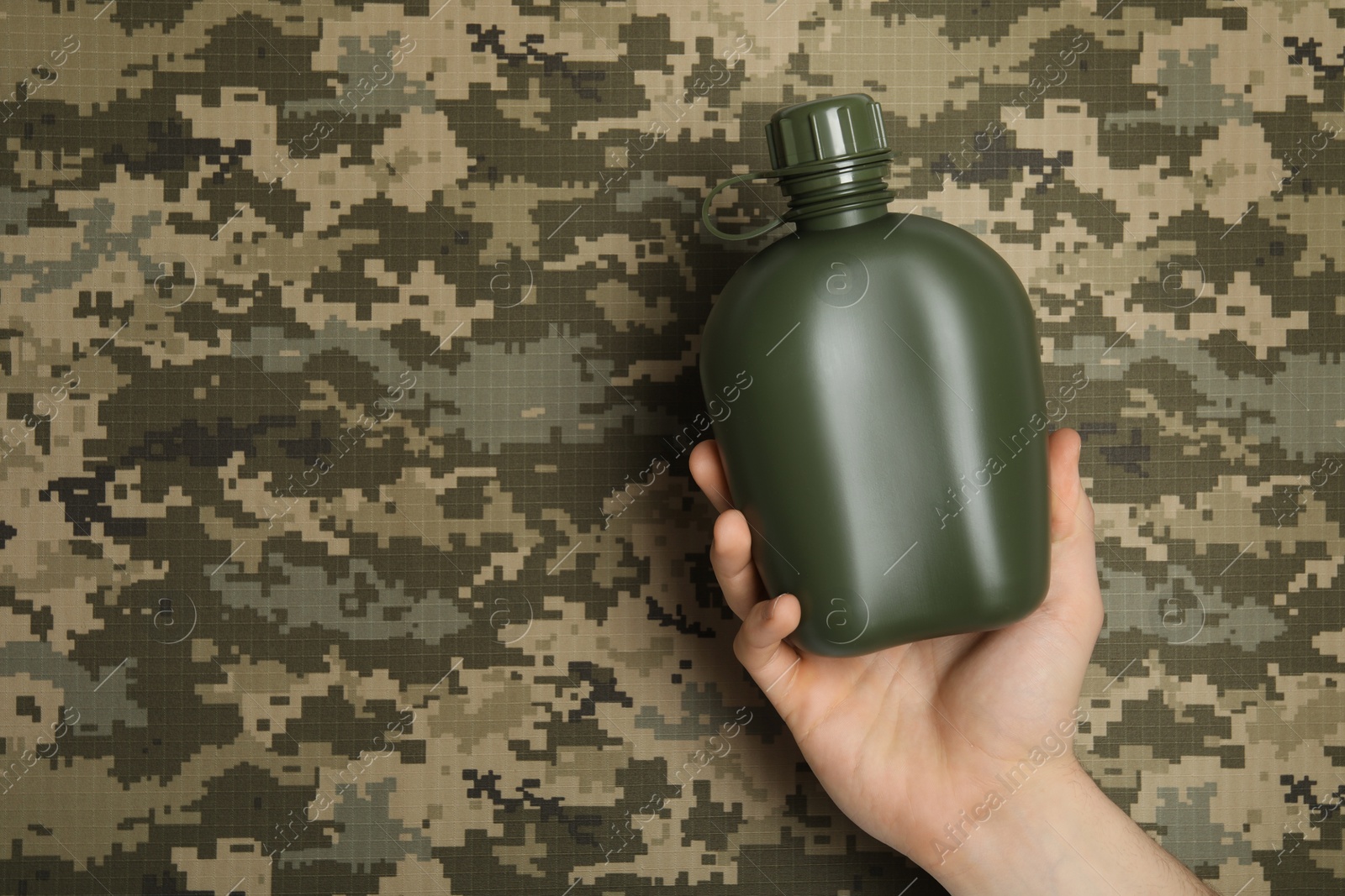 Photo of Man holding green plastic canteen on camouflage background, closeup. Space for text