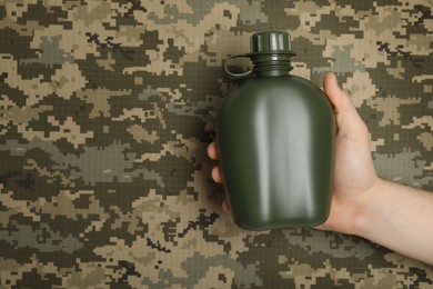 Photo of Man holding green plastic canteen on camouflage background, closeup. Space for text