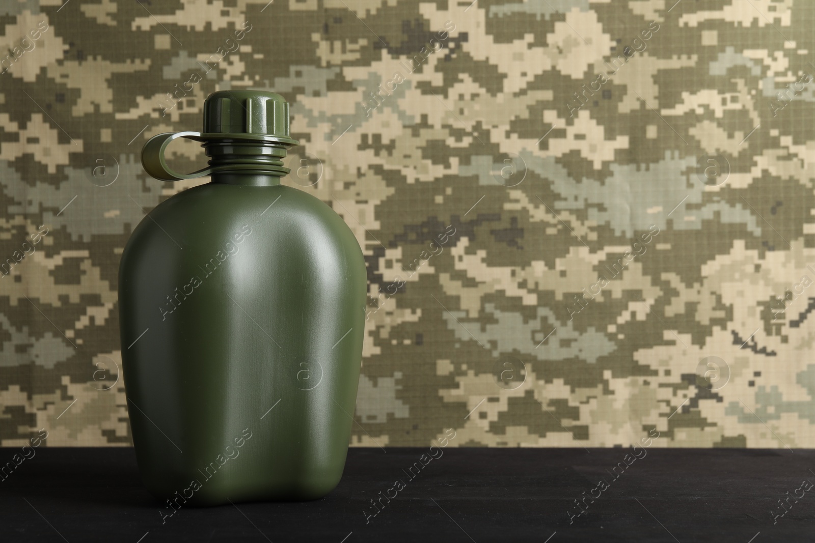 Photo of Green plastic canteen on black wooden table, closeup. Space for text