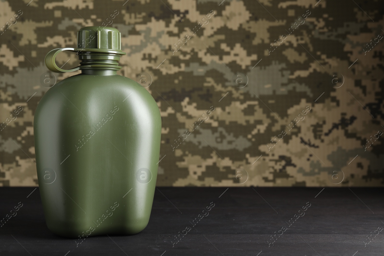 Photo of Green plastic canteen on black wooden table, closeup. Space for text