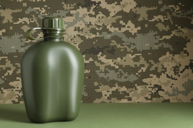 Photo of Plastic canteen on light green table against camouflage background, closeup. Space for text