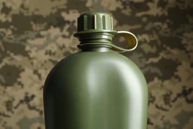 Photo of Green plastic canteen on camouflage background, closeup