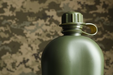 Photo of Green plastic canteen on camouflage background, closeup