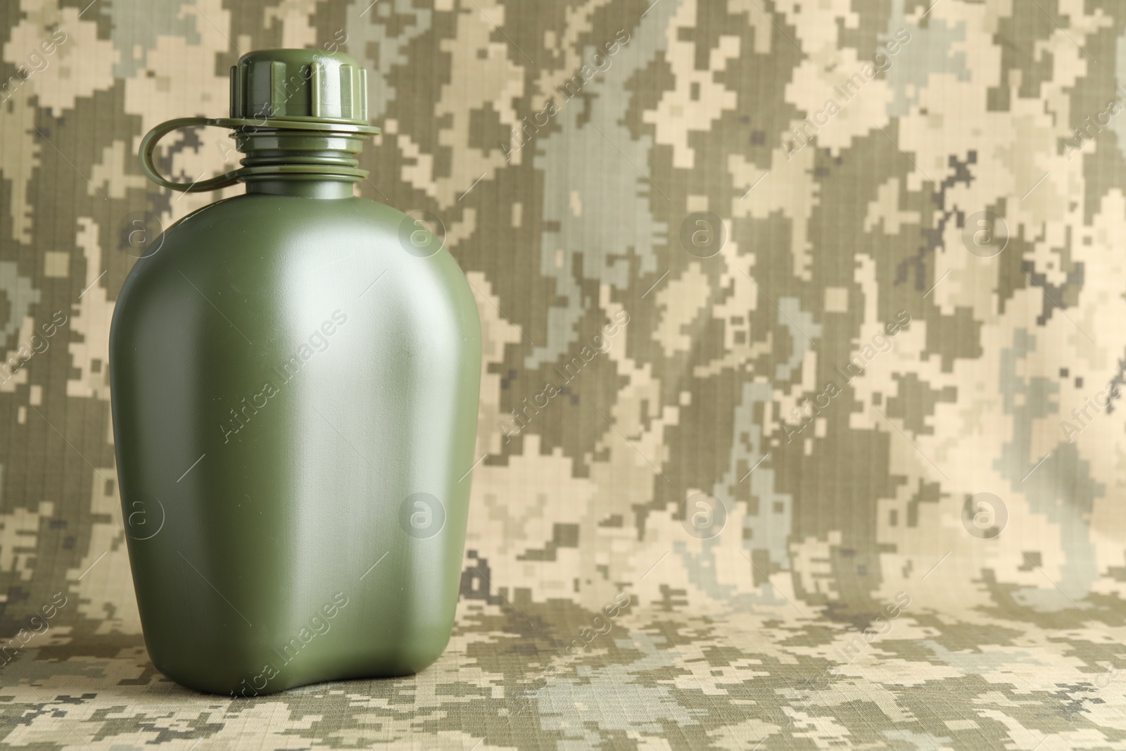 Photo of Green plastic canteen on camouflage background, closeup. Space for text