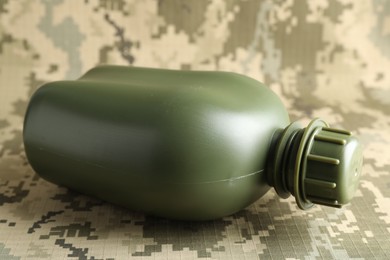 Photo of Green plastic canteen on camouflage background, closeup