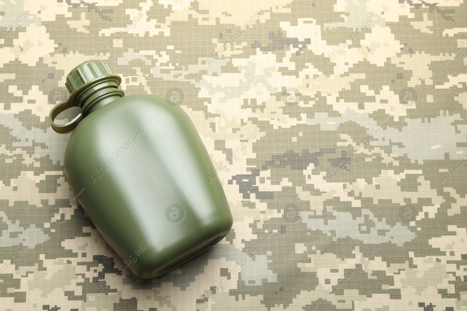 Photo of Green plastic canteen on camouflage background, top view. Space for text