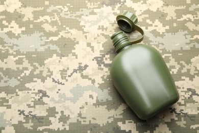 Photo of Green plastic canteen on camouflage background, top view. Space for text