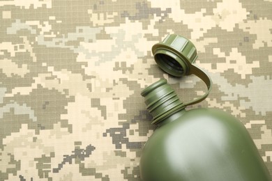 Photo of Green plastic canteen on camouflage background, top view. Space for text