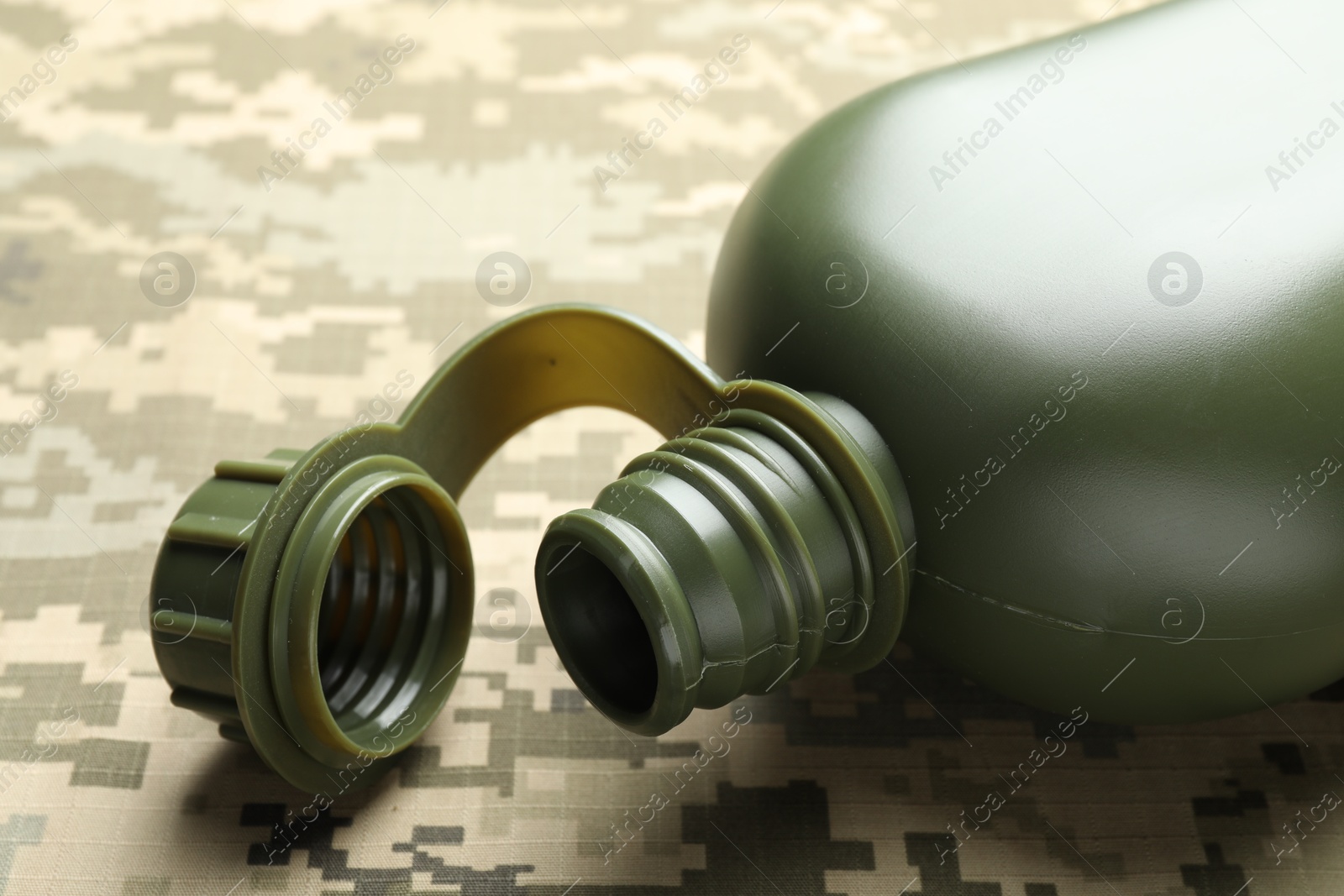 Photo of Green plastic canteen on camouflage background, closeup