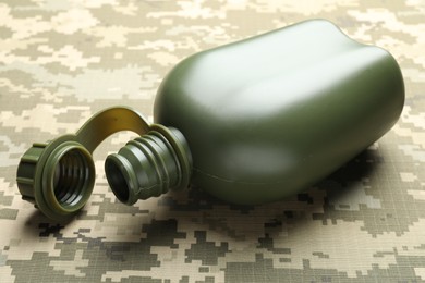 Photo of Green plastic canteen on camouflage background, closeup