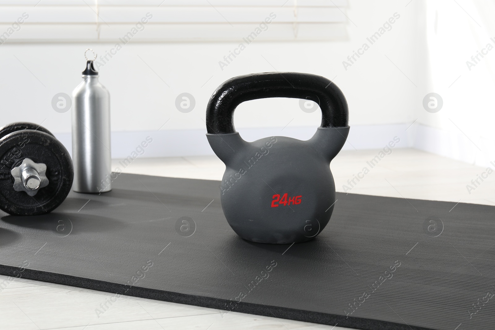 Photo of Kettlebell, barbell, thermo bottle and mat on floor indoors