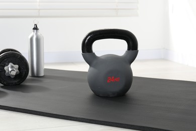 Photo of Kettlebell, barbell, thermo bottle and mat on floor indoors