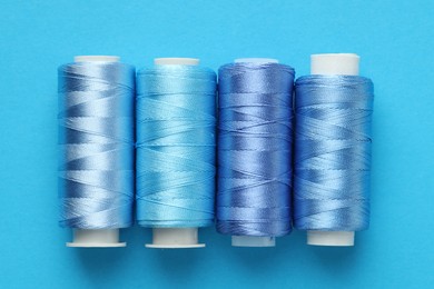 Photo of Spools of sewing threads on light blue background, flat lay