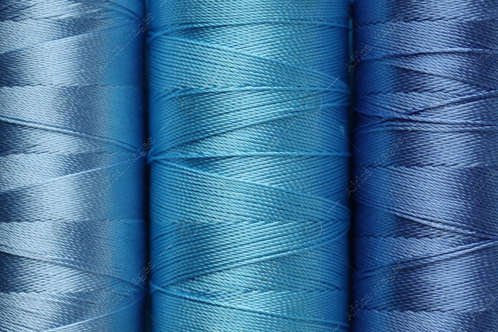 Photo of Spools of light blue sewing threads as background, top view