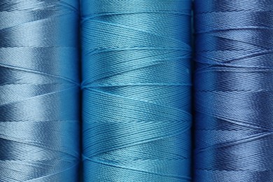 Photo of Spools of light blue sewing threads as background, top view