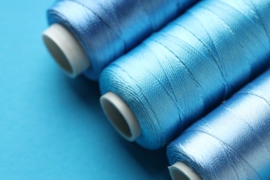 Photo of Spools of sewing threads on light blue background, closeup