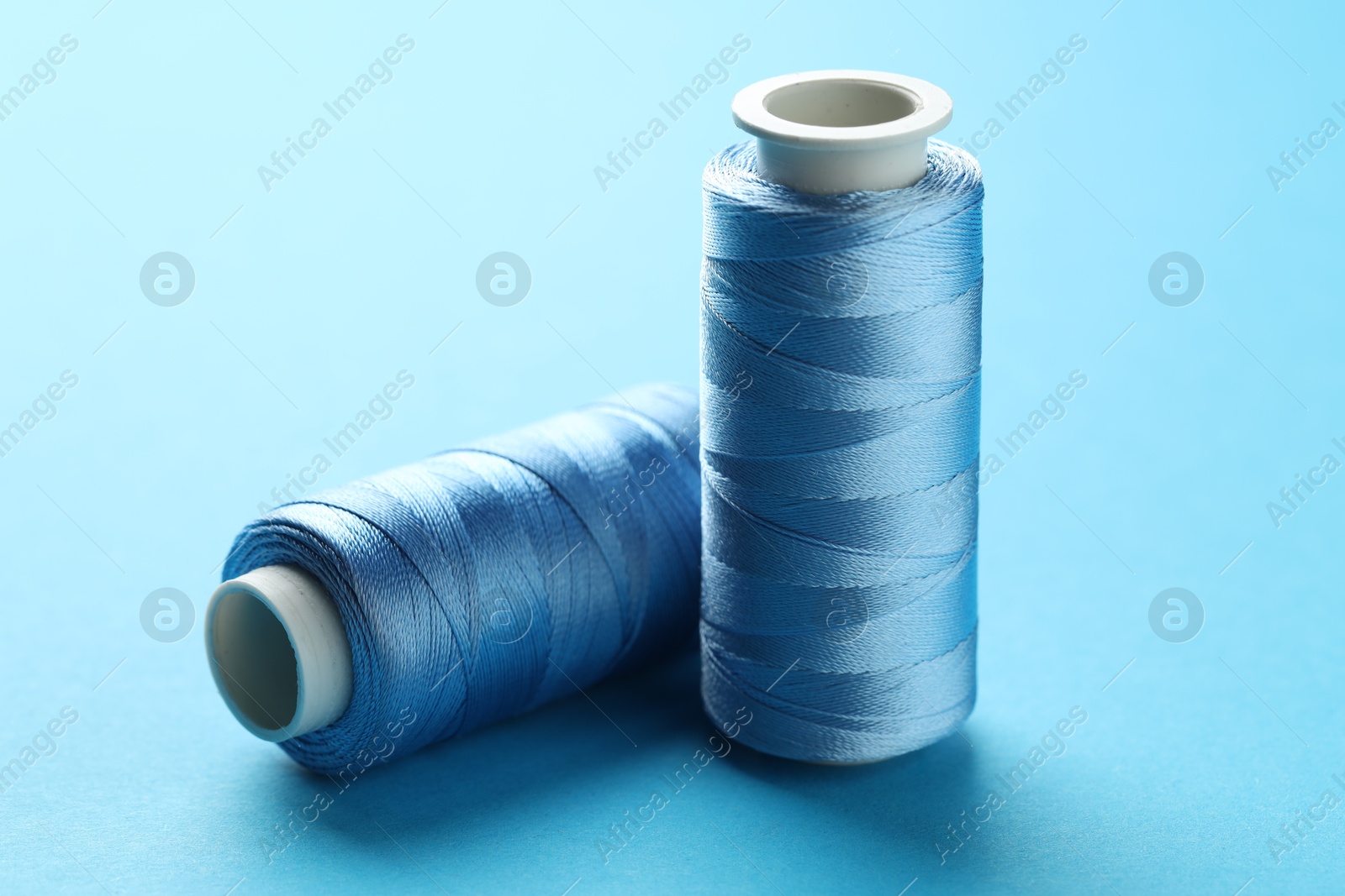 Photo of Spools of sewing threads on light blue background, closeup