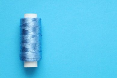 Photo of Spool of sewing thread on light blue background, top view. Space for text