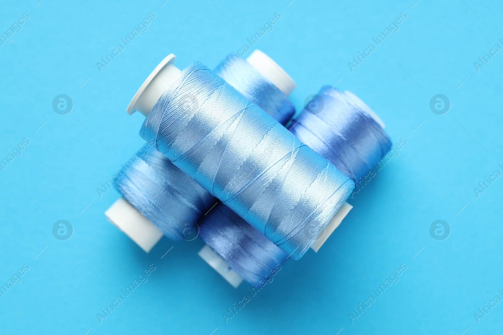 Photo of Spools of sewing threads on light blue background, top view