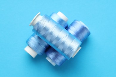 Photo of Spools of sewing threads on light blue background, top view