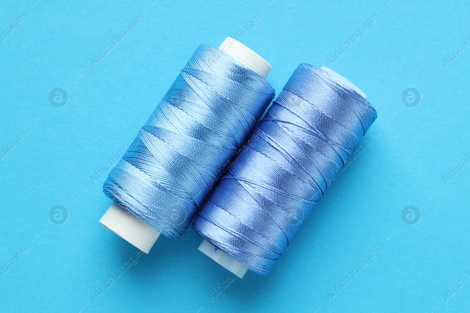 Photo of Spools of sewing threads on light blue background, top view