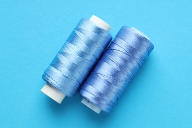 Photo of Spools of sewing threads on light blue background, top view