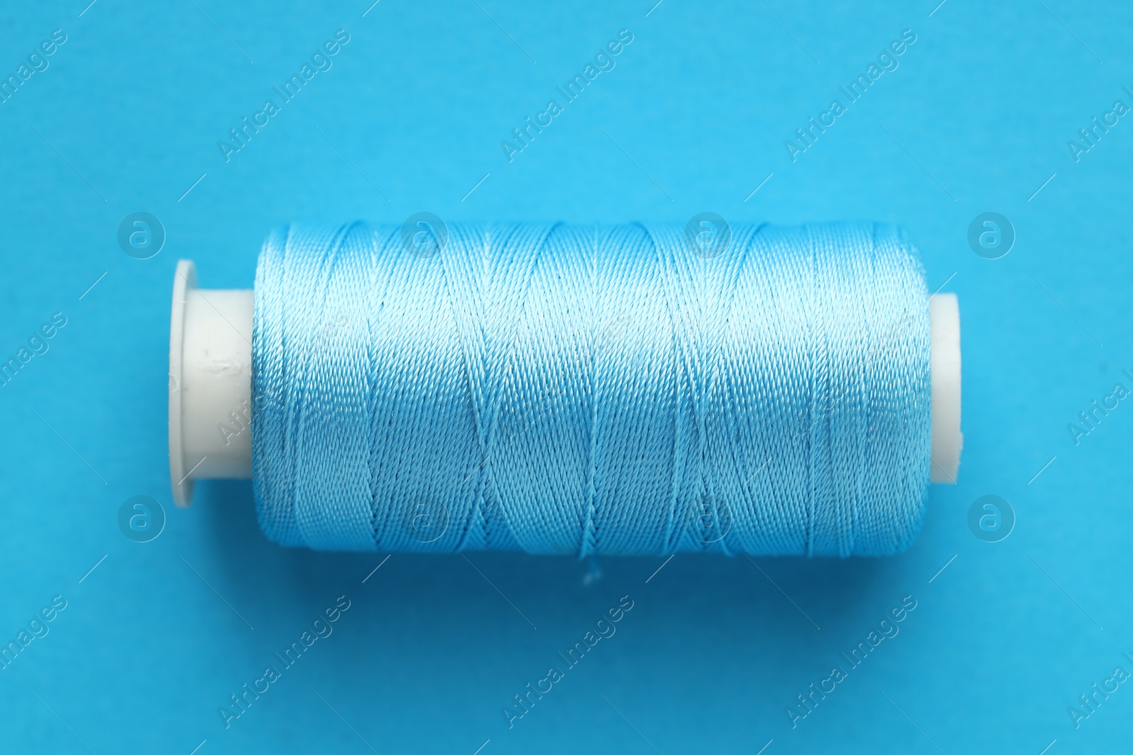 Photo of Spool of sewing thread on light blue background, top view