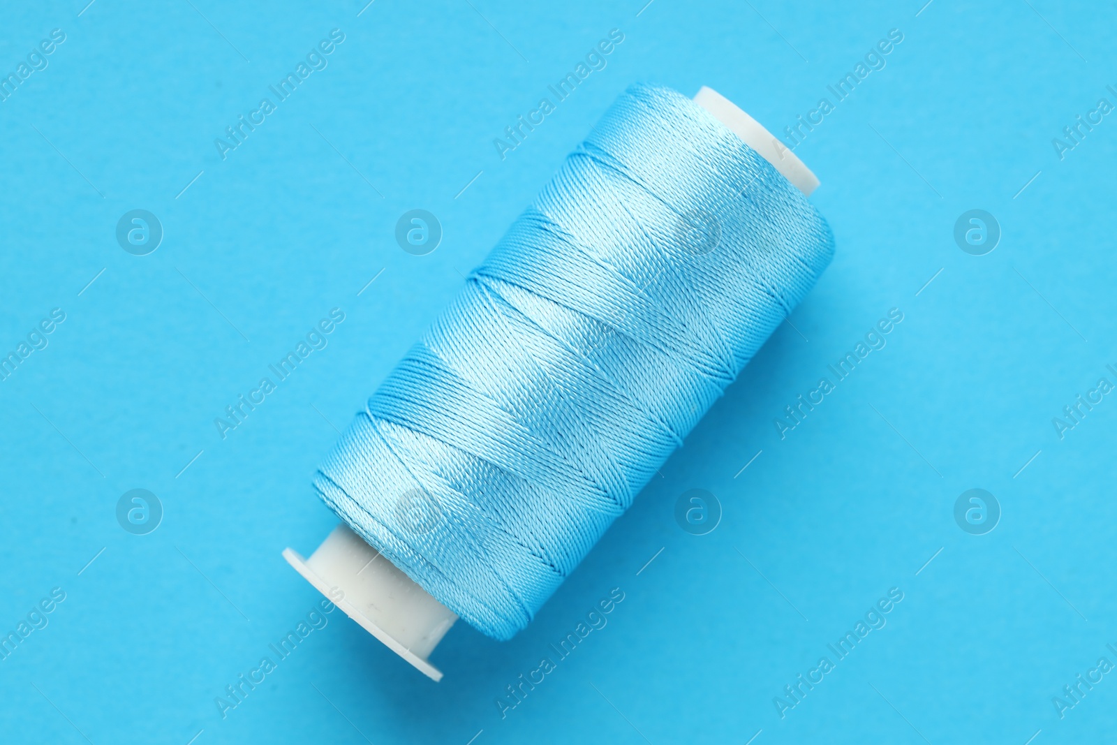 Photo of Spool of sewing thread on light blue background, top view